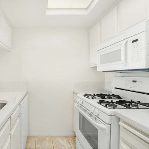 Thumbnail 11 of 28 A white kitchen with a stove, sink, and microwave.