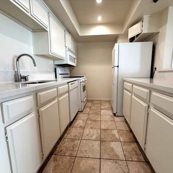 Thumbnail 10 of 24 A kitchen with white cabinets and a tiled floor.
