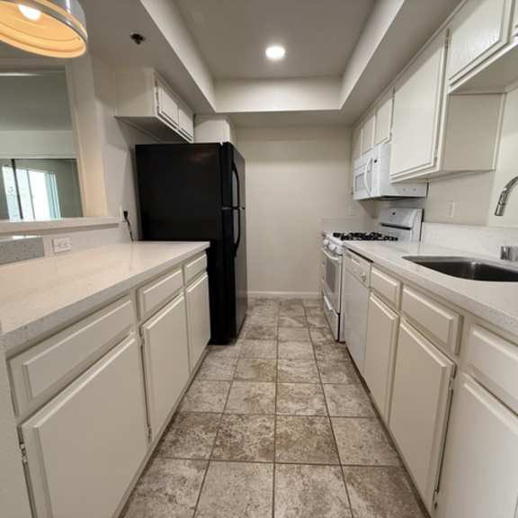 Thumbnail 10 of 15 A kitchen with white cabinets and a black refrigerator.
