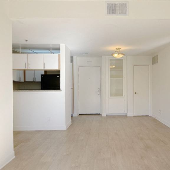Thumbnail 4 of 16 A spacious room with a kitchen area in the background and a doorway leading to another room.
