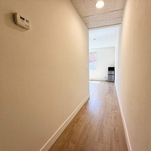 Thumbnail 3 of 13 A long hallway with a white wall and wood flooring.