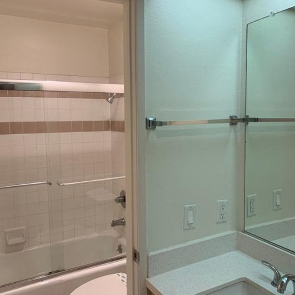 Thumbnail 3 of 7 A bathroom with a white tiled shower and a white sink.