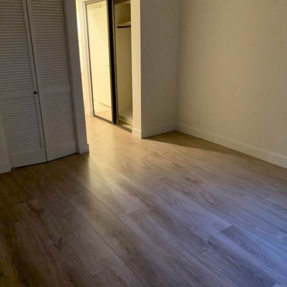 Thumbnail 8 of 8 A room with a wooden floor and a white wall with a door.