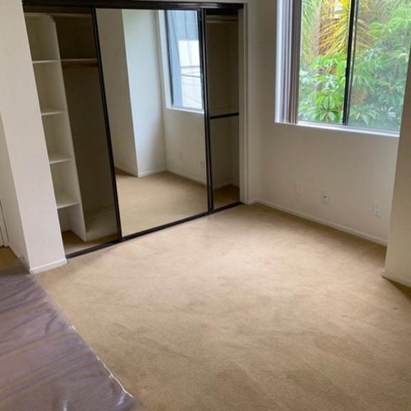 Thumbnail 17 of 27 A room with a carpeted floor, a sliding glass door, and a window showing greenery outside.