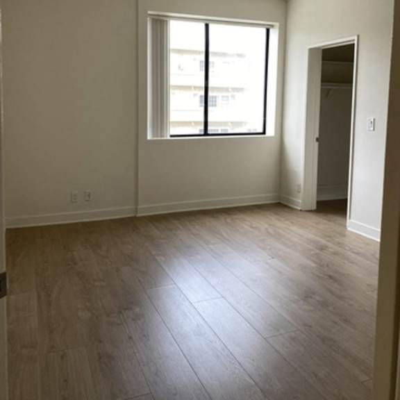 Thumbnail 6 of 10 A room with a window and wooden flooring.