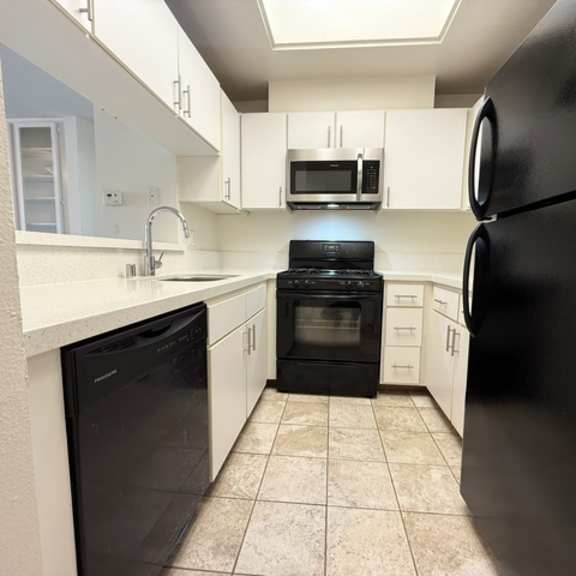 Thumbnail 14 of 44 A black refrigerator is in the corner of a kitchen with white cabinets and a black dishwasher.
