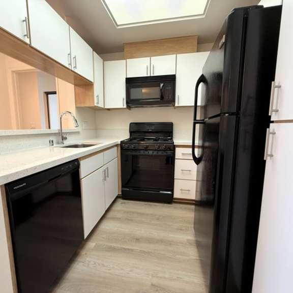 Thumbnail 4 of 26 A black refrigerator stands in a kitchen with white cabinets and black appliances.