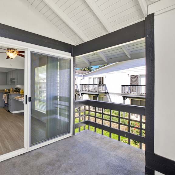 Thumbnail 9 of 18 A balcony with a glass railing and sliding glass doors leading to a kitchen.