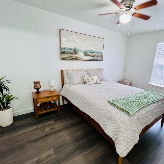 a bedroom with a bed, a ceiling fan, and a painting on the wall.