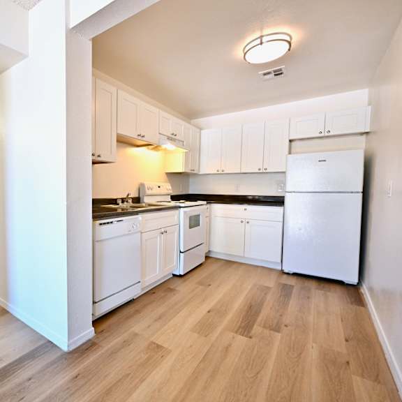 a kitchen with white appliances and wooden floors.