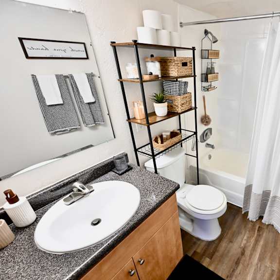 a bathroom with a white shower curtain, a white toilet, a sink, and a shelf with baskets and plants.