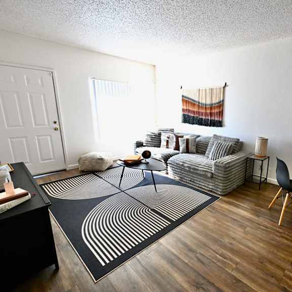 a living room with a black and white rug, a grey sofa, a black dining table and chairs, and a wooden floor.