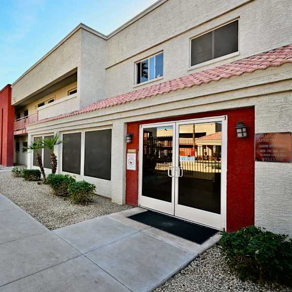 a building with a red door and windows is surrounded by palm trees.