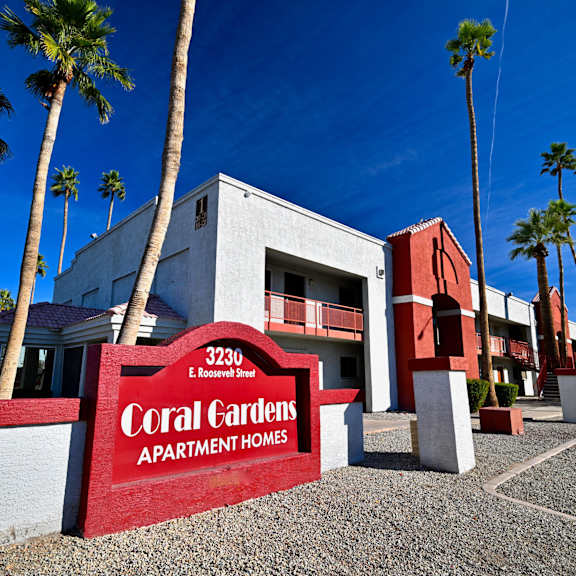 a sign for coral gardens apartment homes is in front of a building with palm trees.