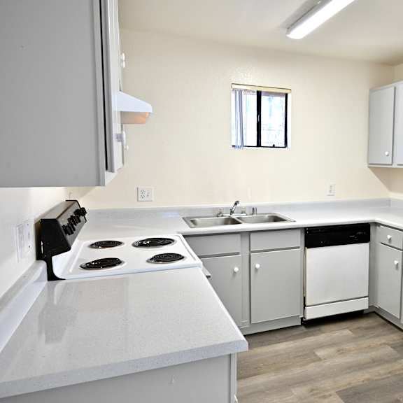 a white kitchen with a stove, sink, and refrigerator.