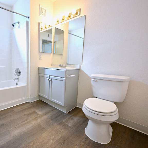 a white toilet sits in a bathroom with a white tub and a white cabinet.