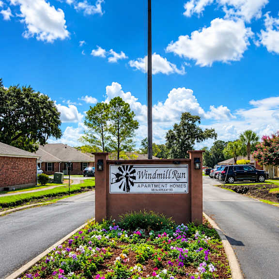 the entrance to windmill run apartment homes is marked by a sign and an american flag.