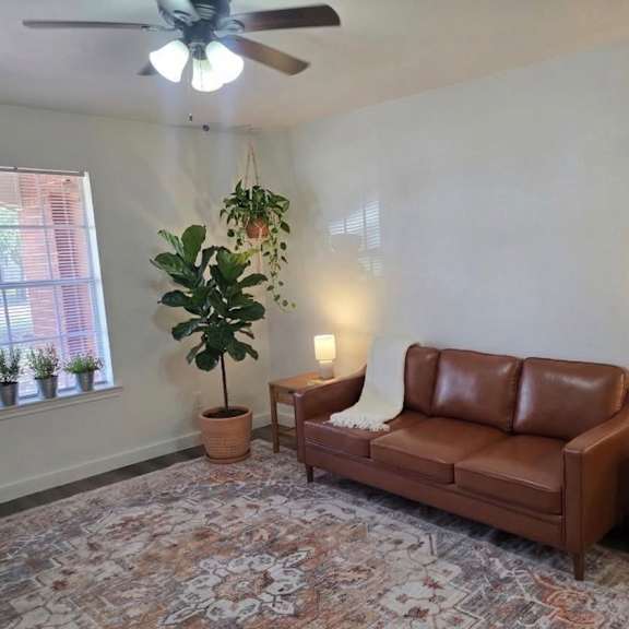 a living room with a brown leather couch, a ceiling fan, and a rug.
