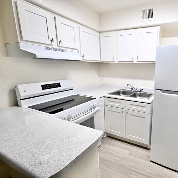a white kitchen with a refrigerator, sink, and oven.