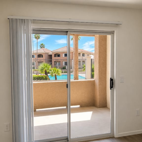 a room with a sliding glass door leading to a balcony with a pool and palm trees.