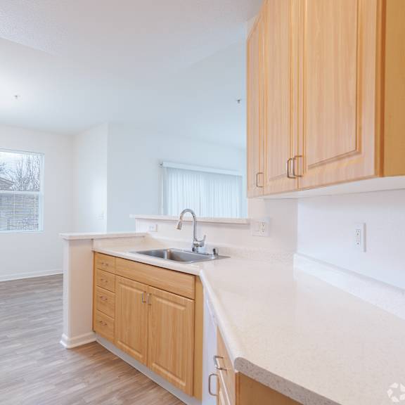 Thumbnail 1 of 2 A kitchen with wooden cabinets and a white countertop.