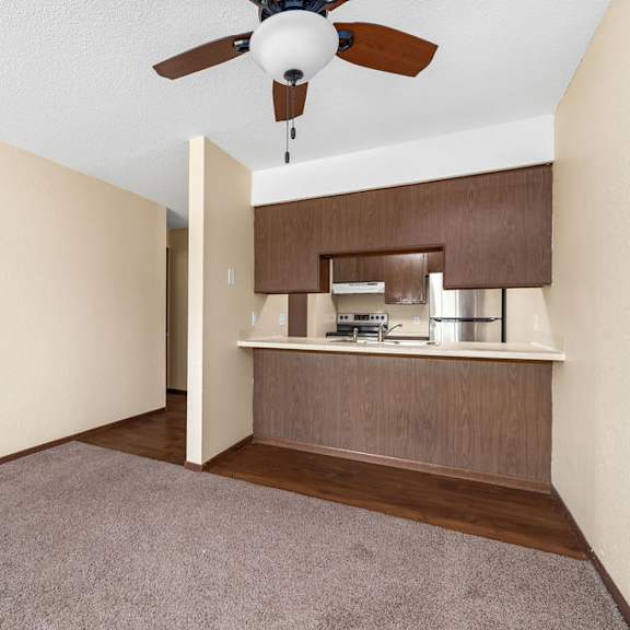 a room with a ceiling fan and a small kitchenette.
