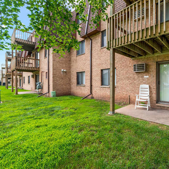 a balcony with two chairs and a table is on the right side of a brick building.