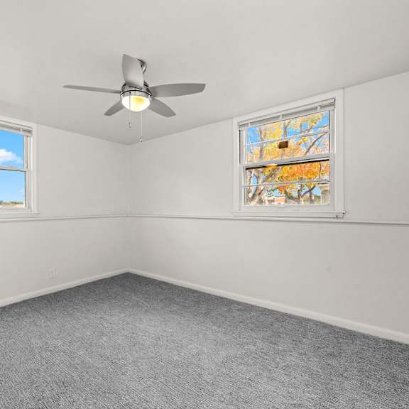 a room with a ceiling fan and two windows.