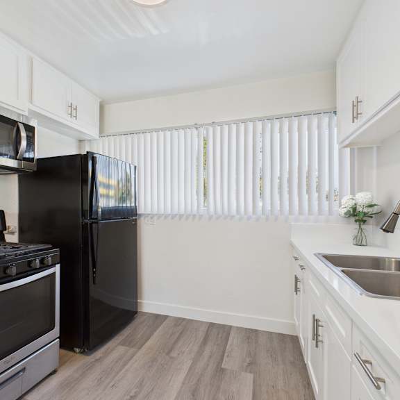 a black refrigerator sits in a kitchen with white cabinets and a stove.