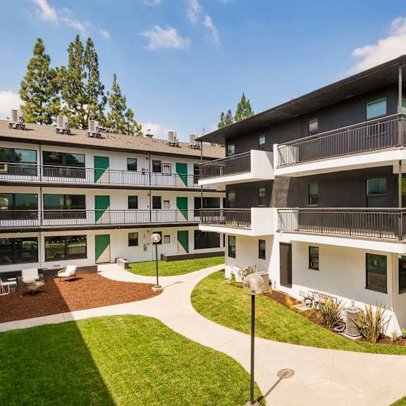 a modern multi-story apartment building with a green lawn in front.