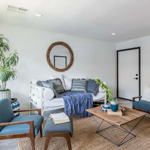 a living room with a white couch, blue chairs, and a painting on the wall.