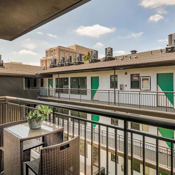 a balcony with a table and chairs overlooks a building with green and white doors.