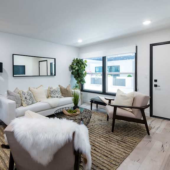 a modern living room with a white couch, a black and white mirror, a white fur throw, and a brown rug.