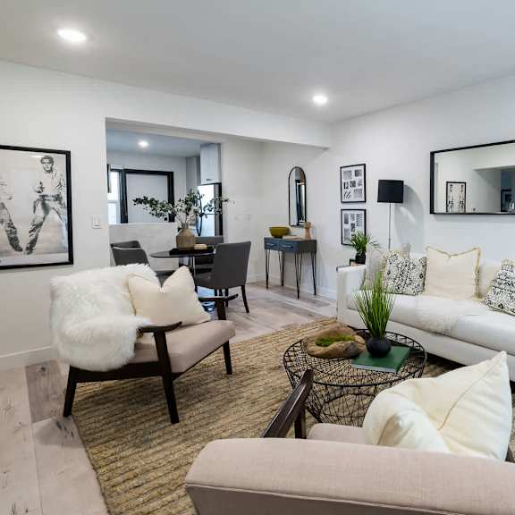 a living room with a white couch, a chair with a white fur throw, and a coffee table with a plant on it.