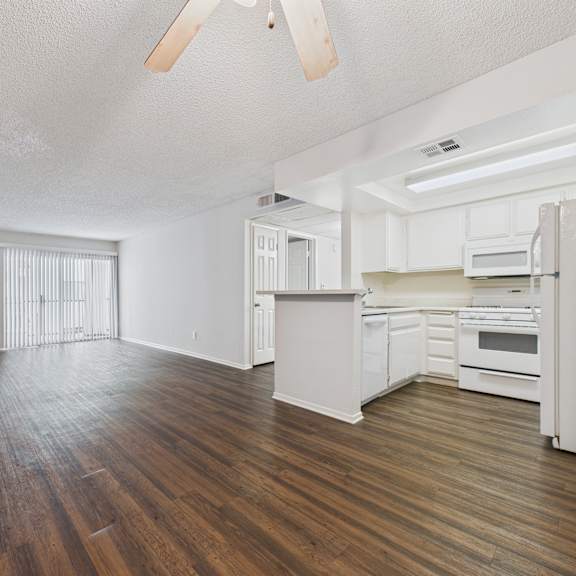 a spacious kitchen and living room with white appliances and wood flooring.