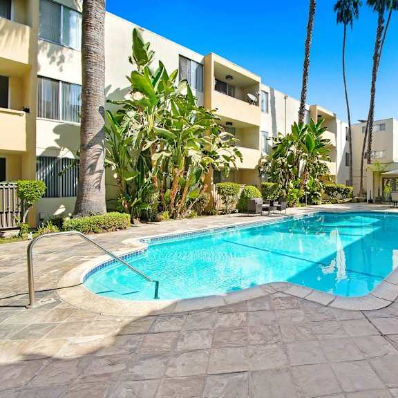 a large swimming pool in front of a hotel with palm trees