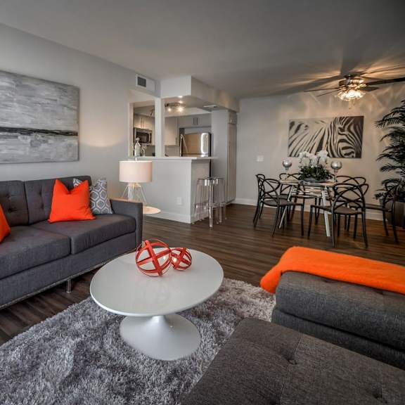 a grey couch with orange pillows sits in a living room with a white coffee table in front of it.