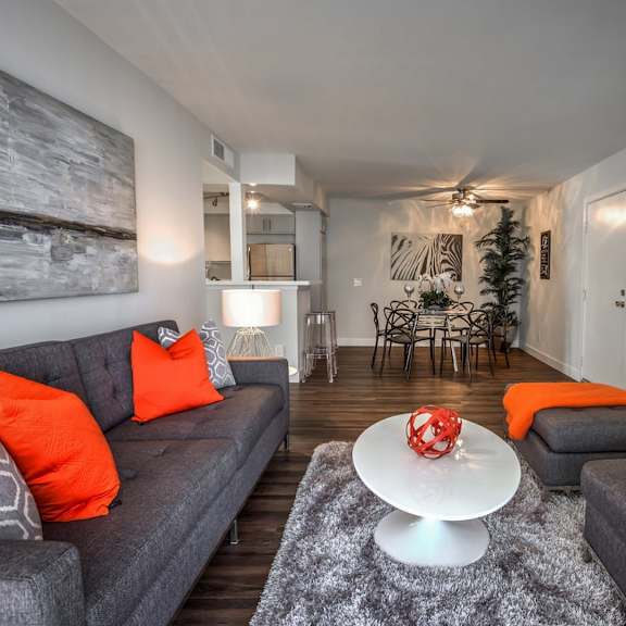 a living room with grey couches and orange pillows.