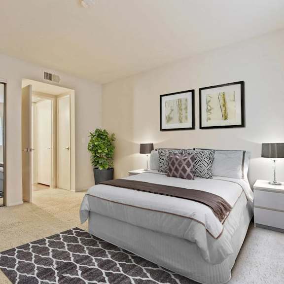 a bedroom with a large bed, a nightstand with a lamp, and a plant in the corner.