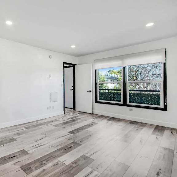 a room with white walls and wooden flooring with a view of trees outside the window.