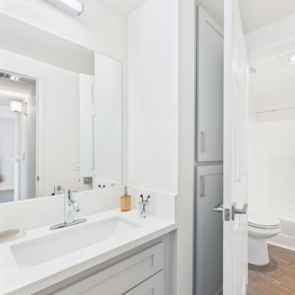 a white bathroom with a sink, mirror, toilet and shower.