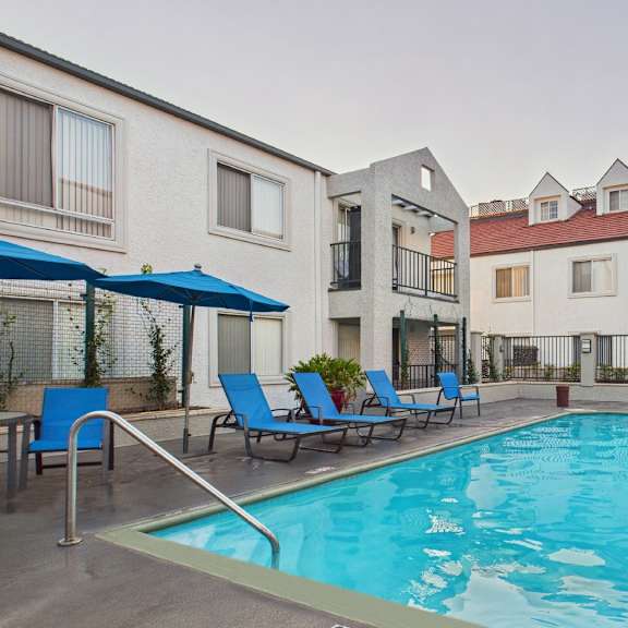 a swimming pool surrounded by lounge chairs and umbrellas in front of a building.