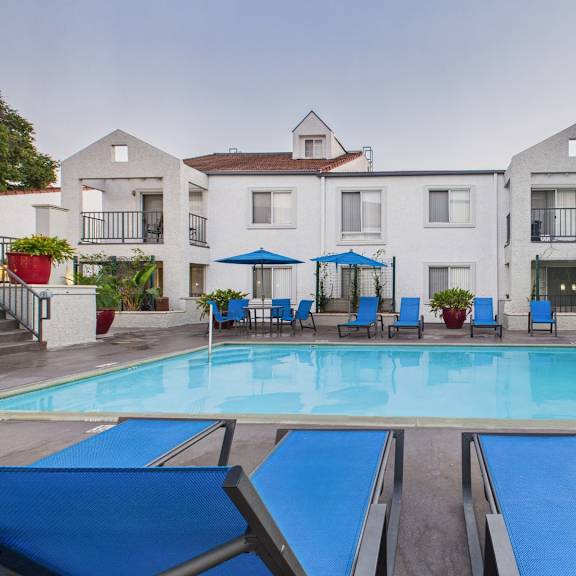 a pool with sun loungers in front of apartment buildings.