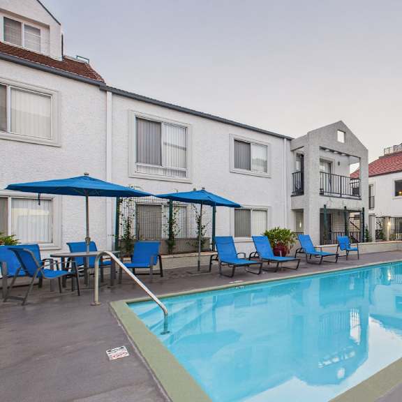 a swimming pool surrounded by chairs and umbrellas in a residential area.