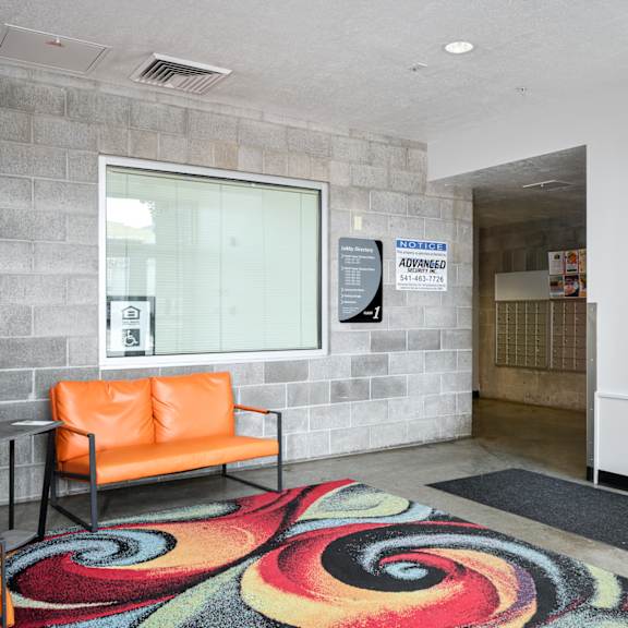 a lobby with orange chairs and a colorful rug and a window