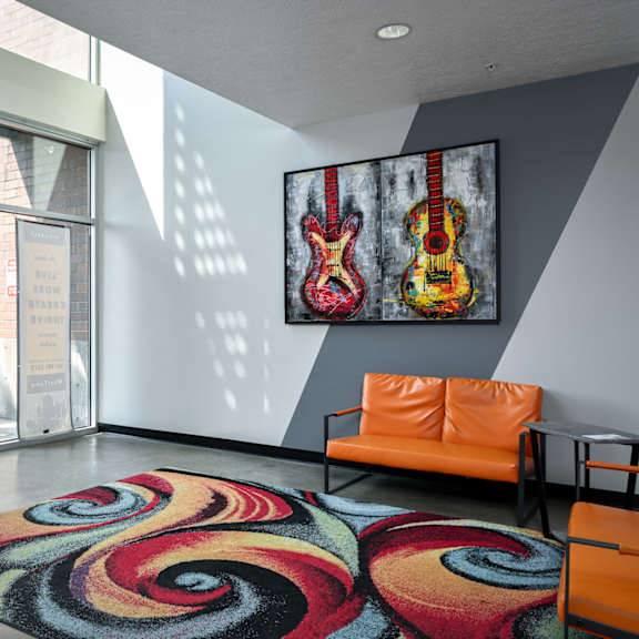 a living room with a colorful rug and a guitar painting on the wall