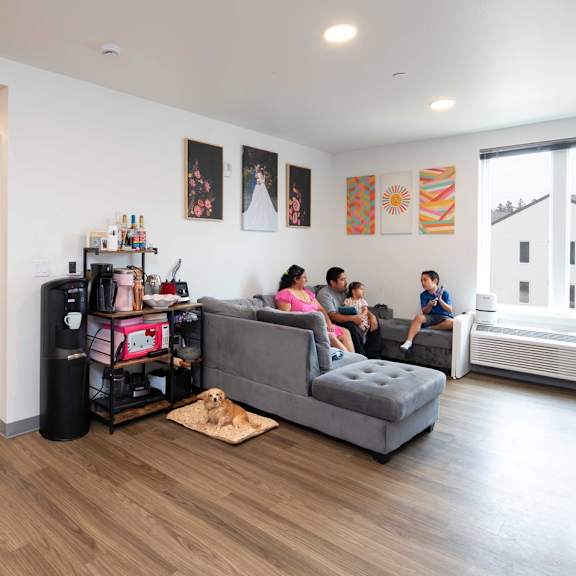 a family is sitting on a couch in a living room with a dog on a rug.