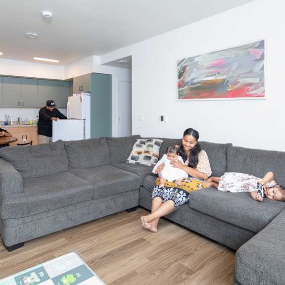 a woman is sitting on a couch with a baby and a child, while another person is in the background.