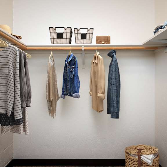 a closet with clothes hanging on the wall and a wooden shelf on the ceiling
