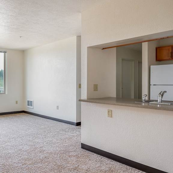 an empty living room with a kitchen and a large window